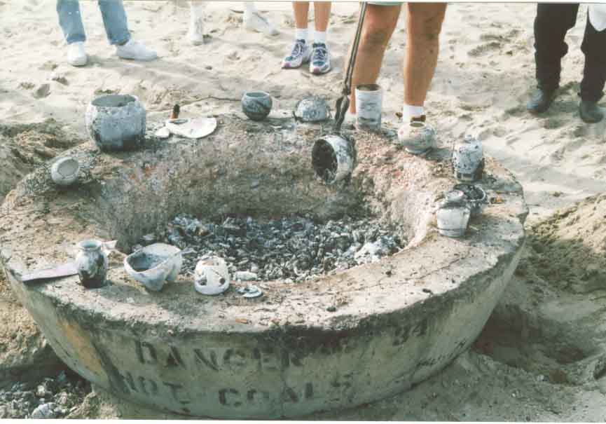 Fired pottery is removed from the pit with tongs